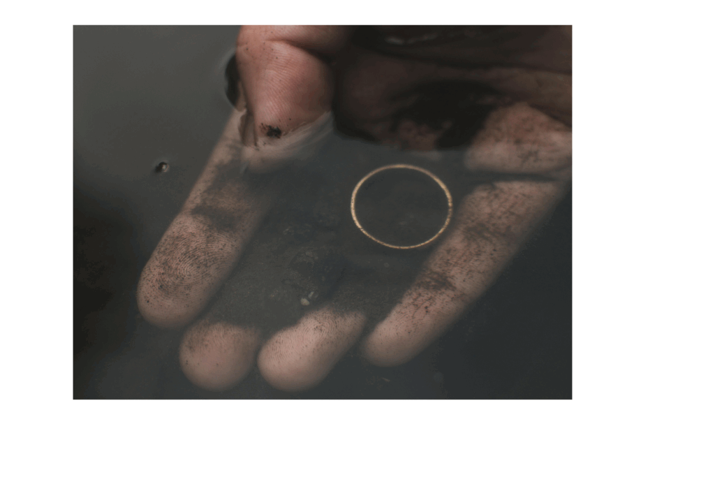 A hand lifting a wedding ring from dirt and water, symbolizing love and resilience in times of crisis